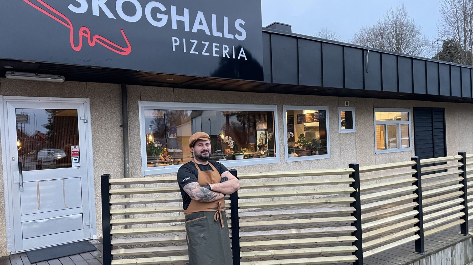 Skoghalls Pizzeria: den svarta skylten med den röda pizzabiten över entrén, uteserveringen framför